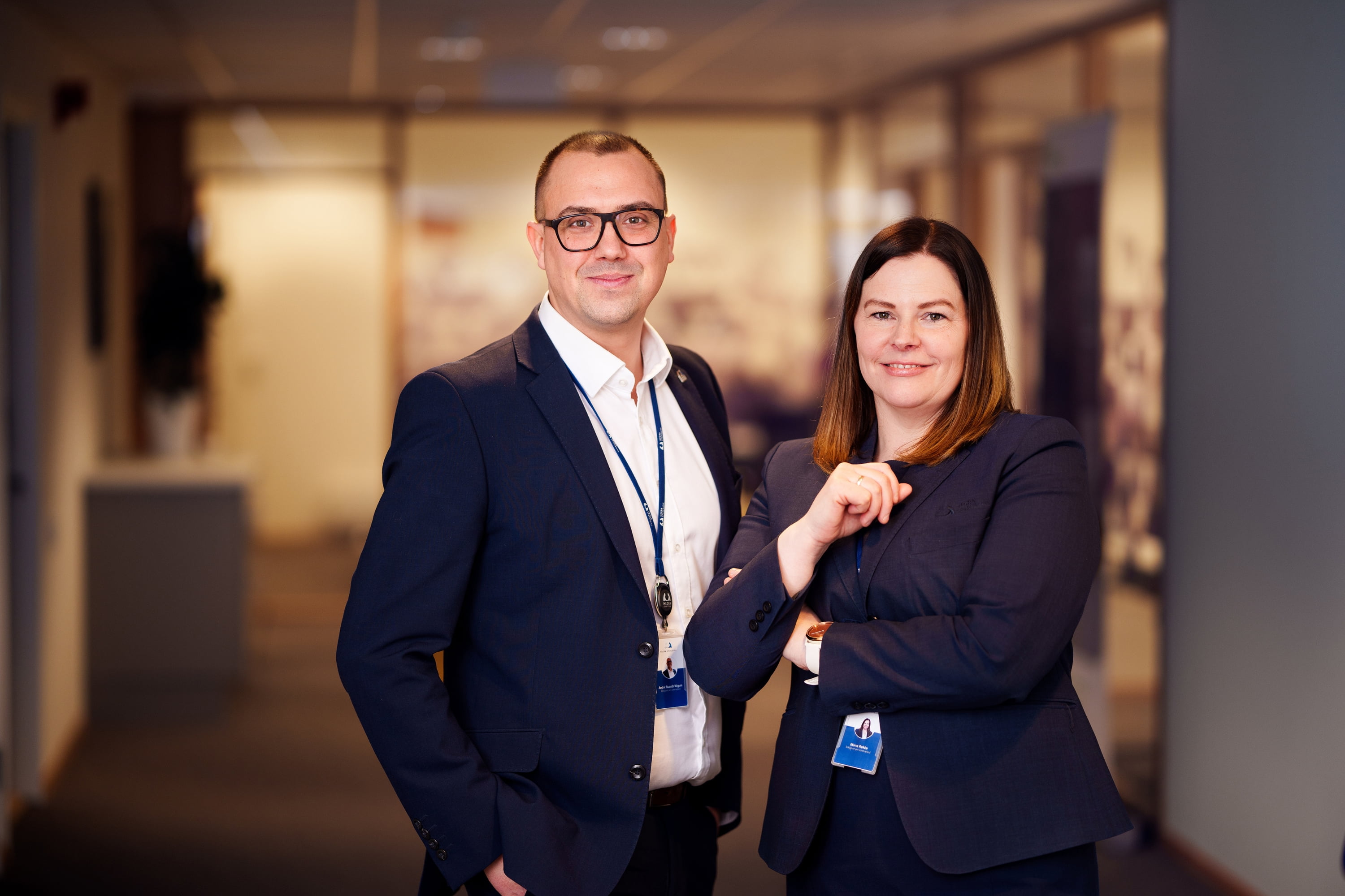 To medarbeidere fra Finanshuset Hegra Sparebank ser inn i kameraet og smiler.