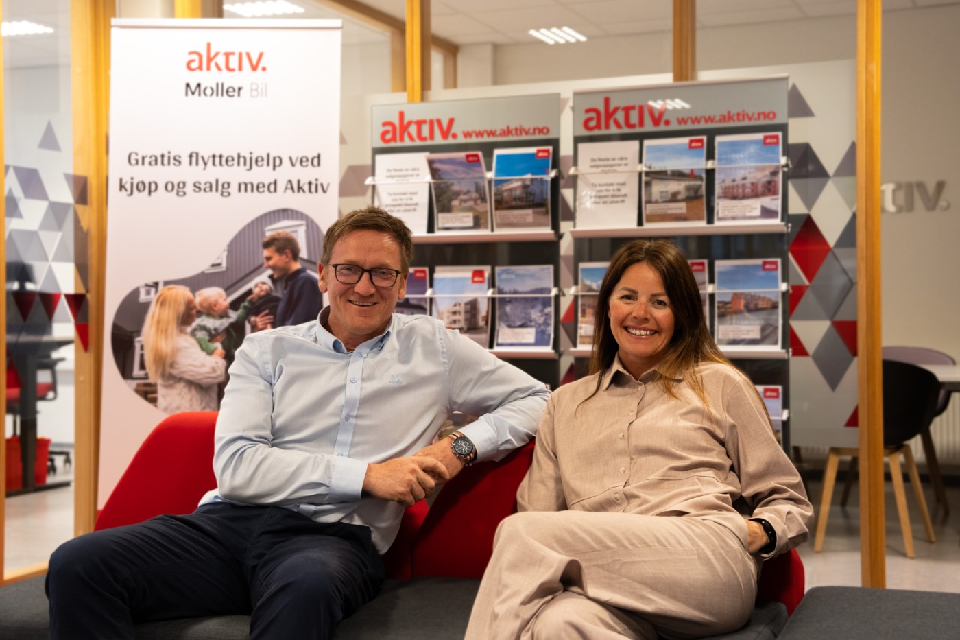 Lars Valstad og Janita Nonstad sitter avslappet i en rød sofa i Triangel park, Finanshuset, smiler og ser fornøyd ut til kameraet