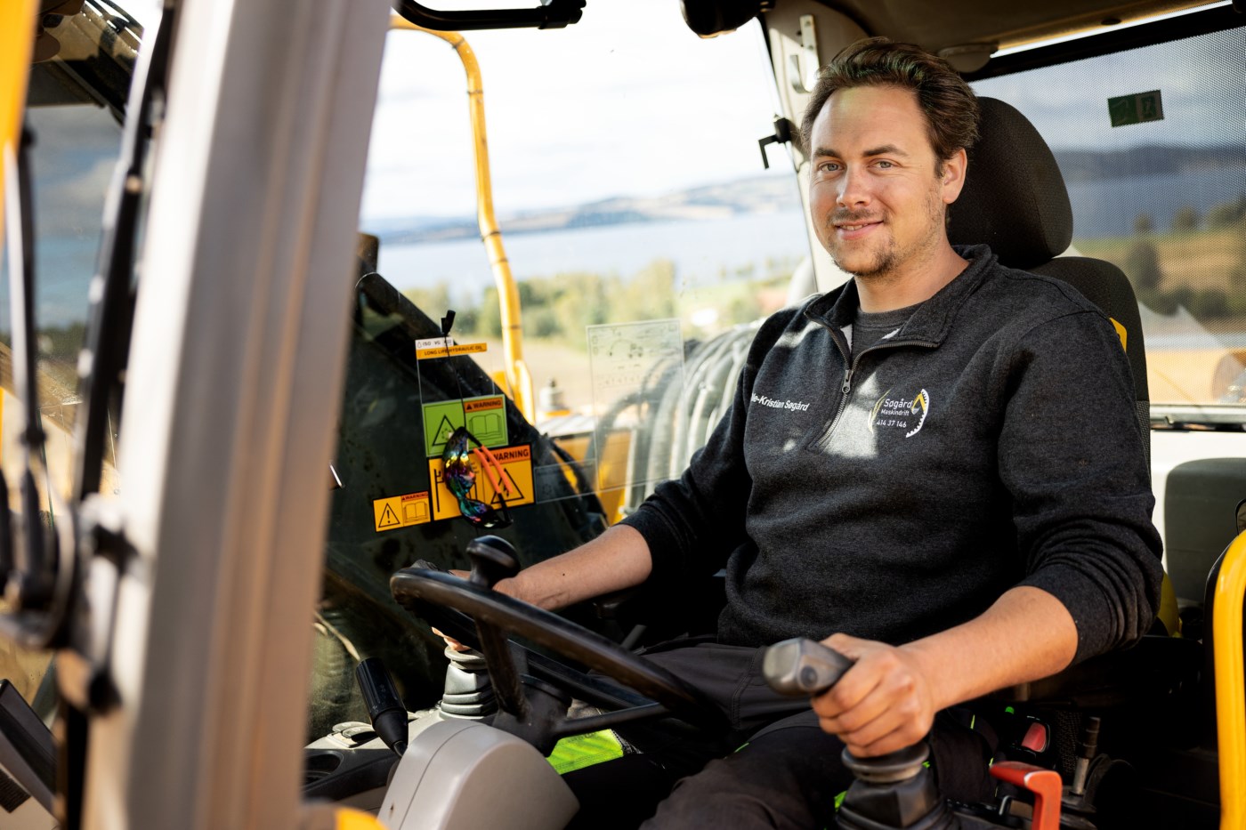 En mann sitter i en gravemaskin og ser på kameraet