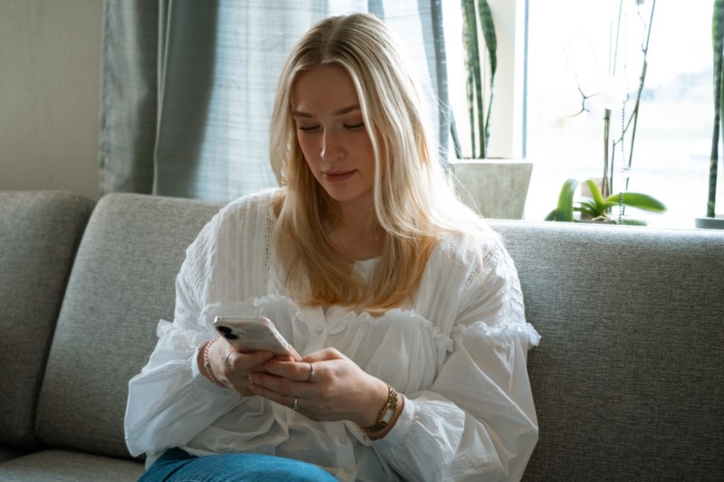En ung dame sitter med mobilen i hendene