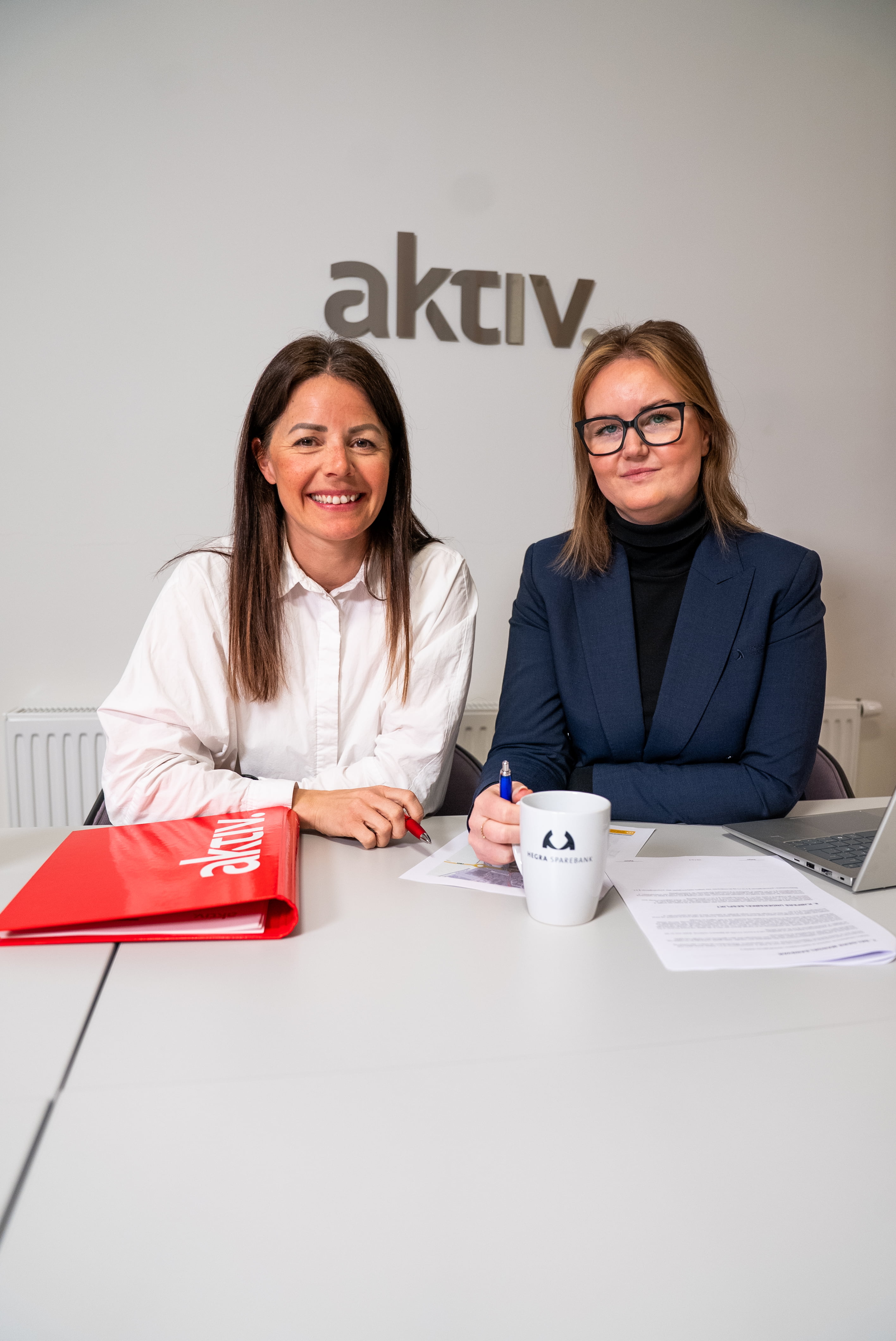 To ansatte i finanshuset hegra sparebank ser mot kamera tilfreds