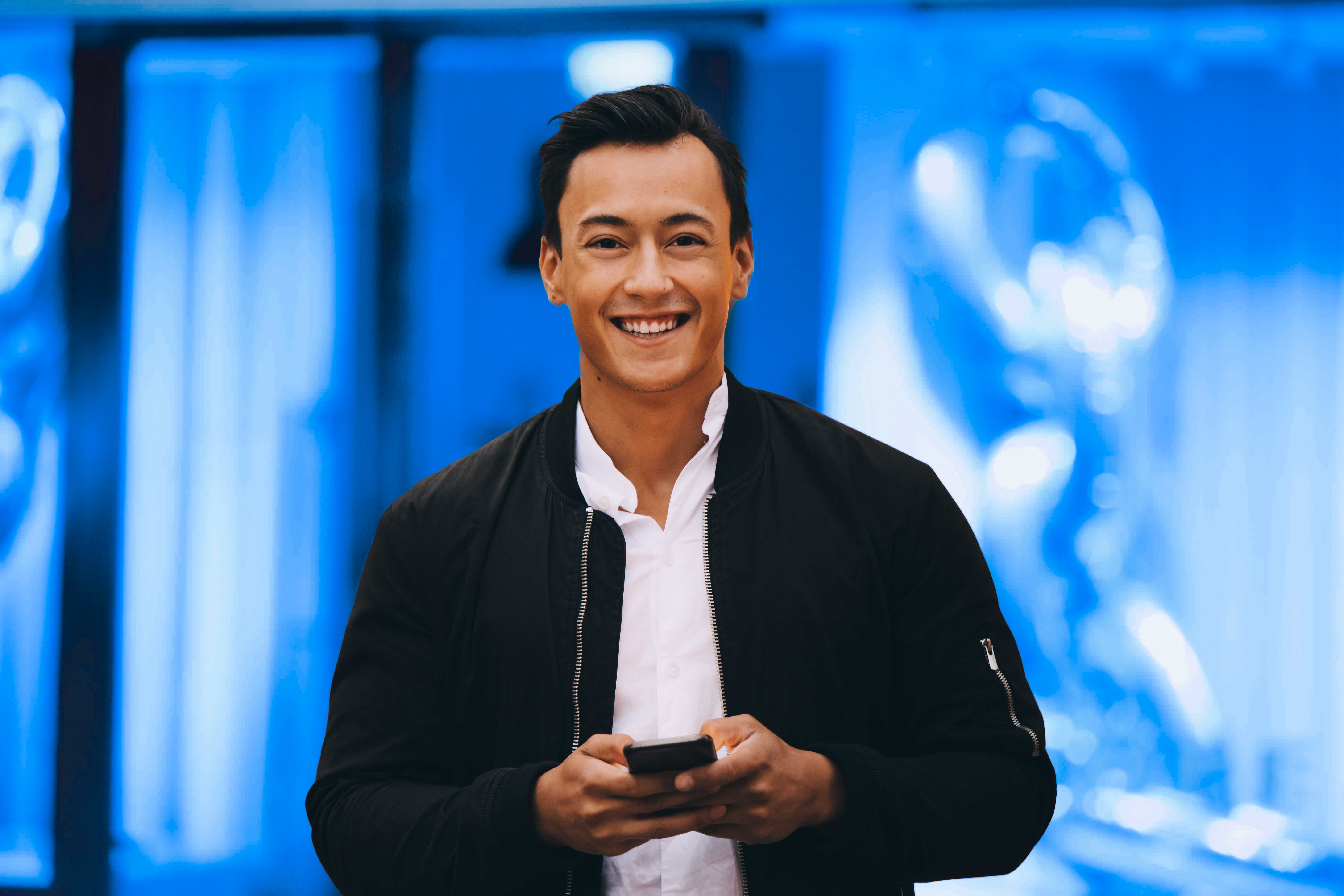 En blid mann med telefonen i hånden som smiler mot kameraet