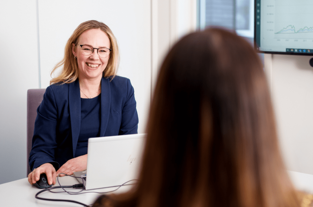 kvinne smiler bak laptop med bakhodet av en annen kvinne i forgrunn