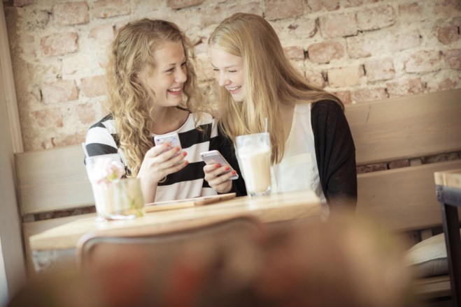 To jenter på kafé ser sammen på mobilen. foto